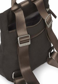 Bruine stoffen rugzak met verstelbare satijnen bandjes, zilverkleurige metalen gespen, voorvak met ritssluiting en een gladde textuur. Heeft een minimalistisch design.