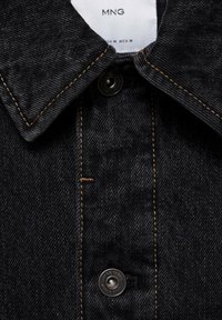 Chaqueta vaquera negra con cuello de solapa, costuras naranjas contrastantes y un botón a presión plateado en la tapeta frontal.