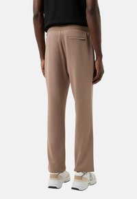 Bruine joggerbroek van zachte stof, met een achterzak en een losse pasvorm, gecombineerd met witte sneakers en een zwarte top.