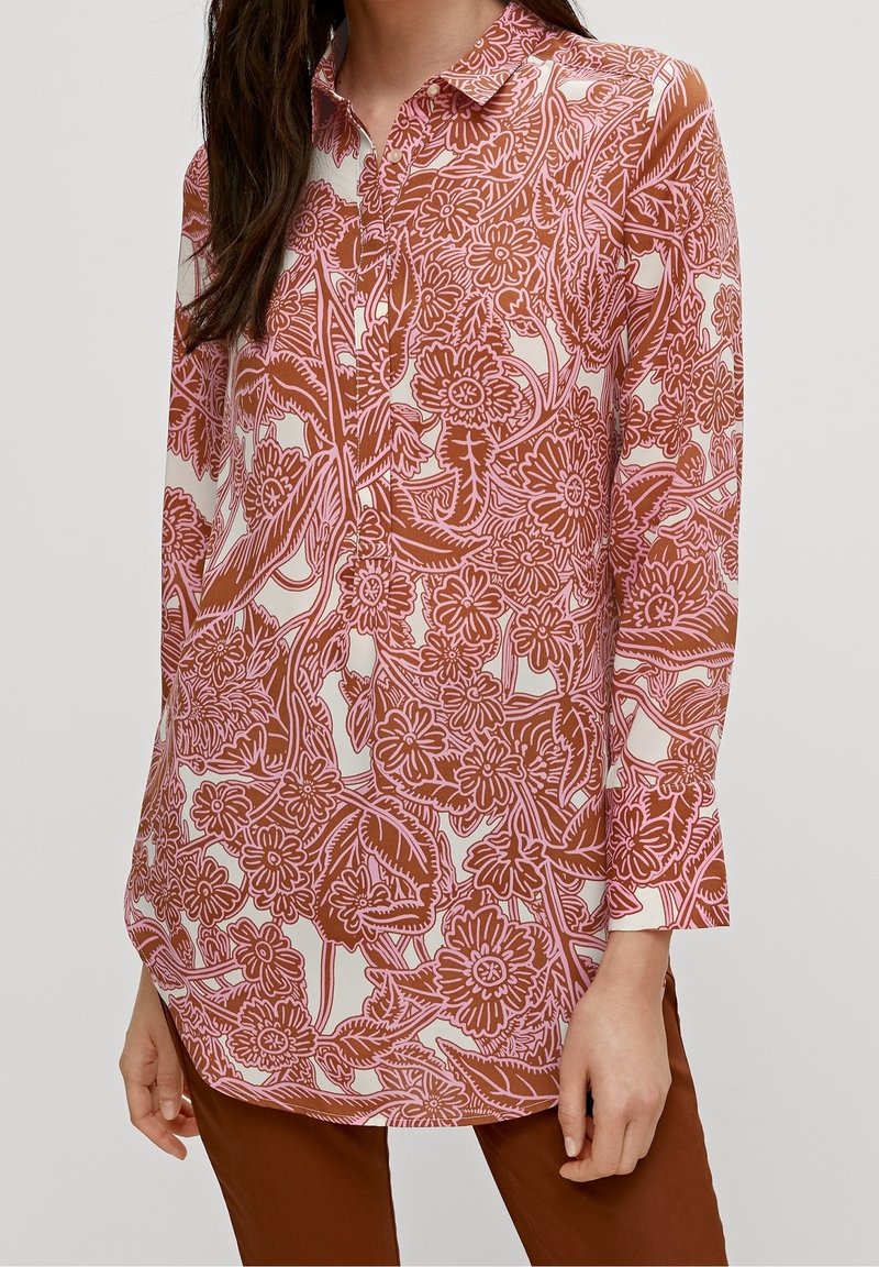 Blusa de manga larga en blanco con intrincados patrones florales en rosa y marrón, con cuello y cierre de botones, y un corte relajado.