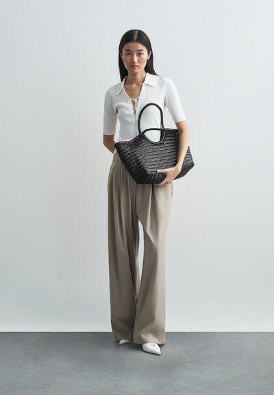 Fekete szőtt táska kerek füllel. A modellen fehér, testhezálló felső és bézs, bő szárú nadrág látható. Simogatós textúra, strukturált forma.
