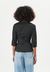 Camicia nera a pois con vita aderente, maniche a tre quarti e polsino abbottonato, abbinata a jeans a gamba larga di colore azzurro chiaro.