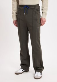 Dark green sweatpants with an elastic waistband and blue drawstring. Side pockets and contrasting stitching. Paired with white and gray sneakers.