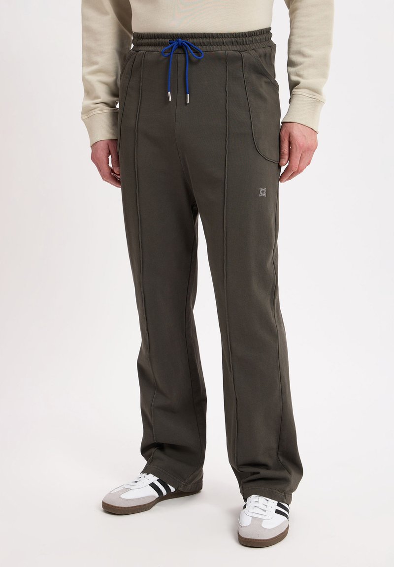 Dark green sweatpants with an elastic waistband and blue drawstring. Side pockets and contrasting stitching. Paired with white and gray sneakers.