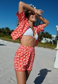 Set da spiaggia a motivo rosso e bianco con maniche corte e pantaloncini a vita elastica, abbinati a un top bikini bianco con trama.