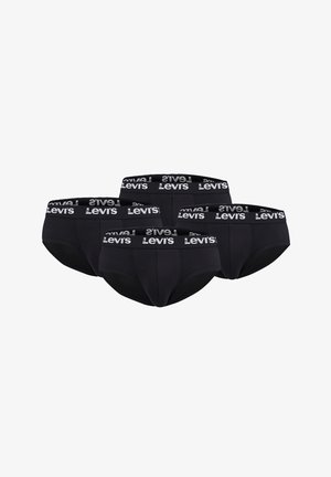 Männliches Model trägt schwarze Levi's Slips mit gebrandetem Bund, zeigt Oberkörper und Beine vor einem einfarbigen hellen Hintergrund.