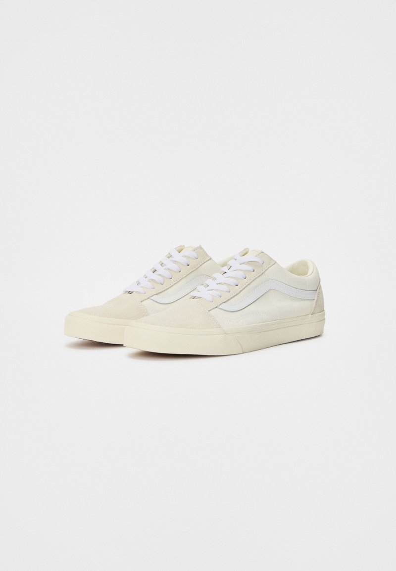 Beige Wildleder-Sneaker mit weißen Akzenten, runder Zehenpartie, flacher Sohle und weißen Schnürsenkeln. Die Seite weist ein markantes Wellenmuster aus leichtem Material auf.