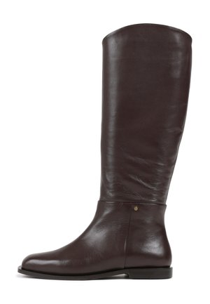Bota alta em couro castanho com textura suave, biqueira arredondada, salto baixo e plano, e um sutil detalhe em dourado perto do tornozelo.