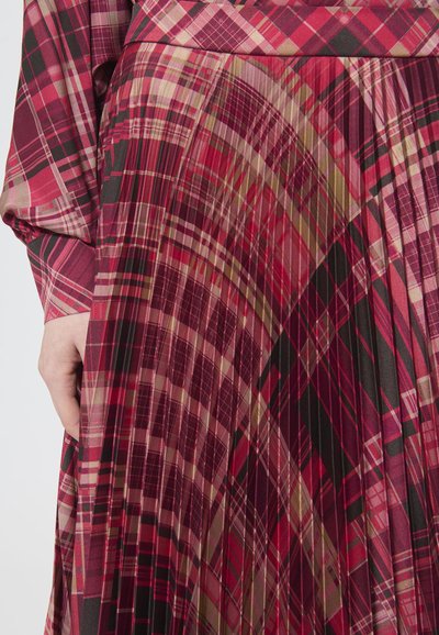 Abito a quadri rosso e rosa, caratterizzato da pieghe e una texture di tessuto fluido. Il motivo include vari design geometrici e accenti di colore.