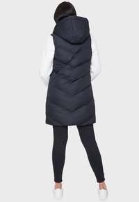 Musta puhvivesti hupparilla, jossa on V-mallinen tikkaus ja sauman yksityiskohtia. Päälle on puettu valkoinen neule ja yhdistetty mustiin leggings-haalareihin.