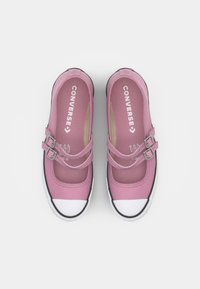 Sapatos Mary Jane de lona cor-de-rosa com duas tiras ajustáveis e biqueiras em borracha branca. Apresenta um contorno preto e a marca "Converse" na parte interior.
