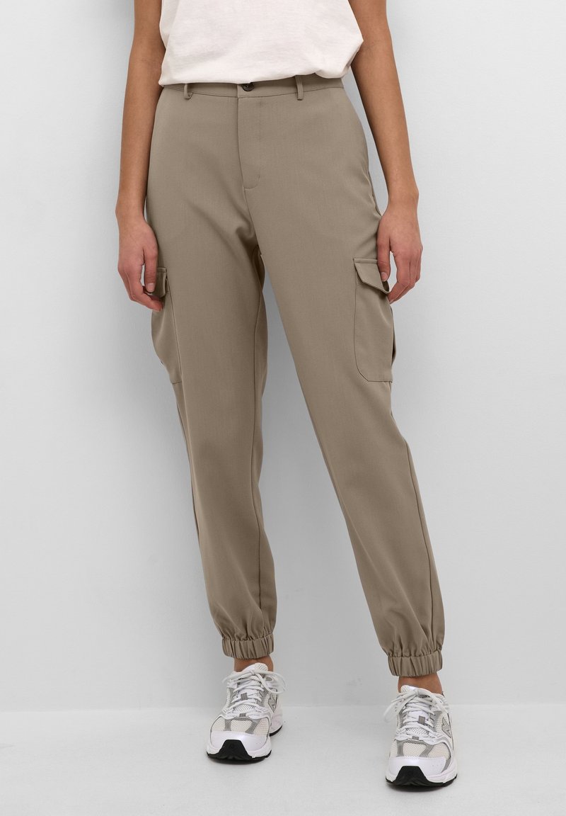 Beige cargobyxor med elastiska muddar, två sidofickor och en slät, jämn tygstruktur. Kombineras med vita sneakers.