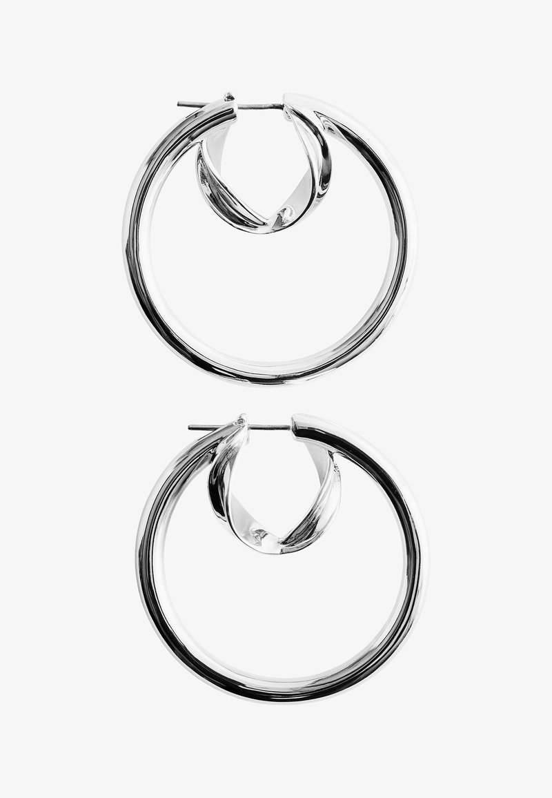 Paire de boucles d'oreilles anneaux en argent poli avec des bords lisses et arrondis et des fermetures à tige, sur fond blanc.