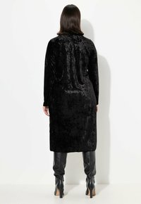 Abito lungo di velluto nero con una texture liscia. Presenta maniche lunghe e una silhouette dritta, abbinato a stivali alti neri in pelle attillati.