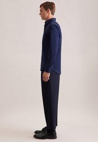 Camicetta azzurro navy a maniche lunghe con colletto strutturato, polsini con bottone e una vestibilità asciutta, indossata con pantaloni scuri su misura e scarpe nere.