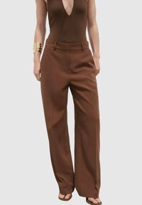 Pantalons amples taille haute marron avec une coupe ajustée, présentant une texture lisse et un subtil pli avant, associés à un haut ajusté.