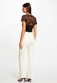 Haut noir avec dos en dentelle, pantalon évasé blanc et escarpins noirs. La dentelle présente des motifs floraux et des manches courtes.