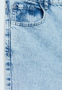 Tissu en denim bleu clair avec une texture délavée. Comprend une petite poche avant et des coutures visibles le long des bords.