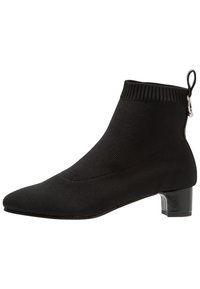 Bottine noire en tricot avec un bout pointu et un petit talon bloc. Elle présente un bord-côtes et une boucle à l'arrière pour un enfilage facile.