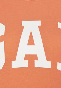 Grande lettre majuscule blanche « A » imprimée sur un fond de tissu texturé orange.