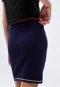 Πλεκτή μωβ μίνι φούστα με υφασμένο σχέδιο καλωδίου, ελαστική μέση και λευκή διακοσμητική λωρίδα στο τελείωμα.