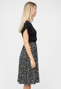 Abito nero a maniche corte con gonna a stampa floreale. La parte superiore ha una texture liscia, mentre la gonna è svolazzante con fiori bianchi e rosa sparsi.