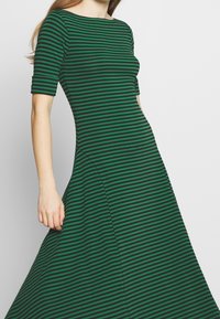 Grön och svart randig klänning med figurnära liv och utställd kjol, med korta ärmar och båtformad urringning, tillverkad av ett mjukt tyg.