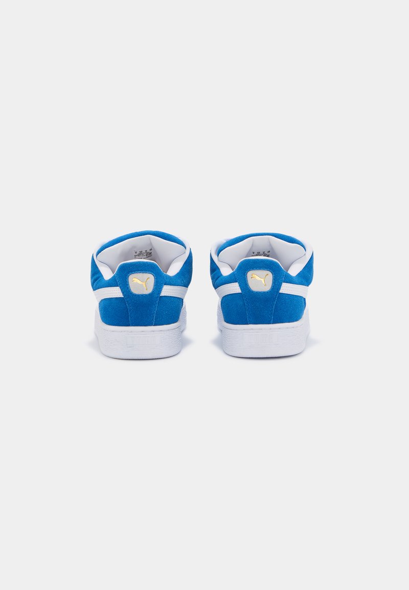 Baskets en daim bleu avec des accents blancs, présentant une semelle texturée et un logo sur le talon arrière. Conçues avec une silhouette basse.