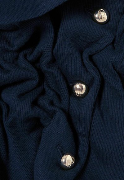 Tessuto blu navy con texture a coste, caratterizzato da bottoni argentati che aggiungono dettaglio. Il materiale è morbido e leggermente stropicciato.