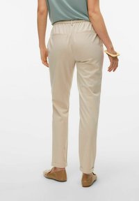 Beige, lichte broek met een elastische tailleband, rechte pasvorm en opgerolde mouwen, gecombineerd met bruine platte schoenen.