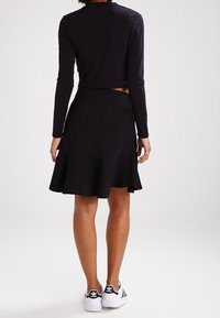 Svart långärmad kort topp kombinerad med en svart utsvängd kjol i mjukt material. Vita sportskor med svarta detaljer.