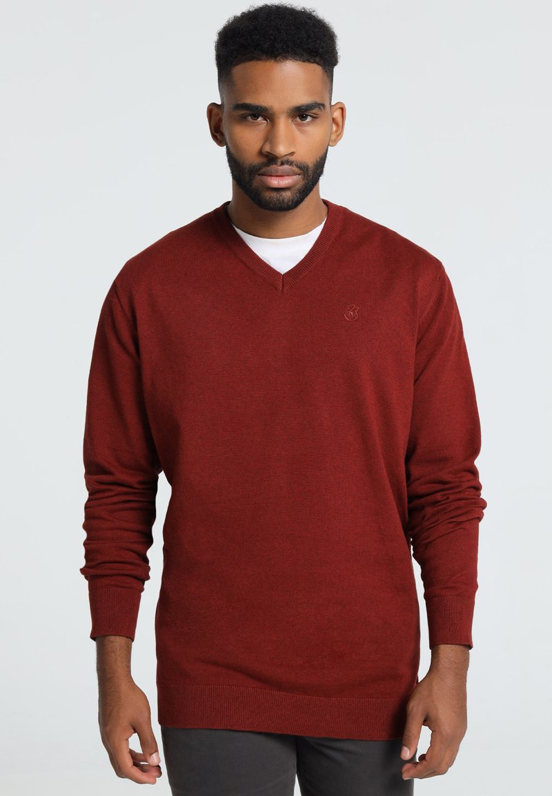 Pull rouge à col en V avec des manches longues, fabriqué en tissu tricoté doux. Il présente un logo subtil sur la poitrine et des poignets et un ourlet côtelés.