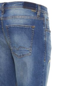Jeans de mezclilla azul con textura desgastada, dos bolsillos traseros con detalles de costura y una etiqueta de marca visible en la cintura.
