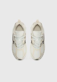 Hvit og beige mesh-sneakers med en teksturert overflate, med svarte akenter, lyseblå skolisser og en løftetapp på tungen.