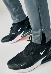 Sorte Nike sneakers har en struktureret overdel og hvidt logo, parret med grå træningsbukser med lynlås ved anklerne.