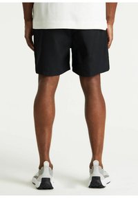 Pantaloni corti neri in tessuto con una texture liscia, caratterizzati da un taglio dritto. Indossati con scarpe da ginnastica grigio chiaro con suole nere.