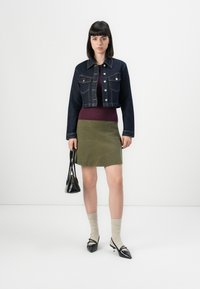 Giacca di jeans cropped con tasche sul petto, maglione a coste borgogna, gonna verde oliva, ballerine nere a punta e una piccola borsa a tracolla nera.