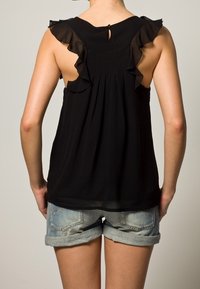 Svart ärmlös topp med volangdetaljer vid axlarna, nyckelhål på baksidan och en lös passform, kombinerad med upplindade jeansshorts.