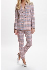 Rosa und blaue kariertes Anzug mit einem doppelt knöpfbaren Blazer und schmal geschnittenen Hosen, ausgestattet mit Taschen und glatter Textur. Weiße High Heels.
