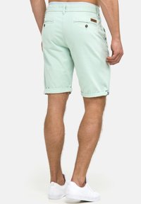 Mintgröna shorts i bomull, med rullade fållar, bakfickor med knappar och en liten varumärkesetikett på midjan.