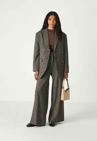 Pilkos dėmėtos kostiumas su ilga švarku ir plačiomis kelnėmis. Po juo vilkimas rudos spalvos marškinėliai ir kreminės spalvos rankinė užbaigia įvaizdį. Avimos juodos plokščios bateliai.