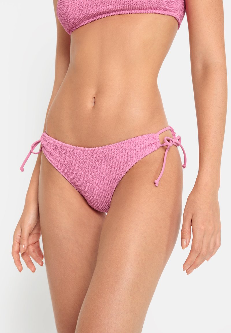 Roza bikini spodnji del iz teksturirane tkanine, z vezalkami na vsaki strani za nastavljivo prileganje. Gladki robovi in nizko sedežna zasnova.