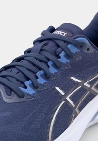Chaussure de sport bleu marine avec une tige texturée, des accents bleu clair contrastants, des lacets plats et une semelle intermédiaire blanche. Présente des détails de logo bien visibles.