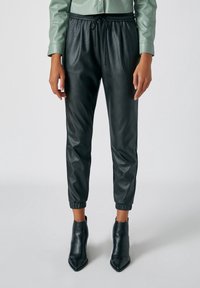 Pantalon jogger noir en cuir avec une taille élastique, un cordon de serrage et des poignets élastiques, associé à des bottines noires à talons pointus.