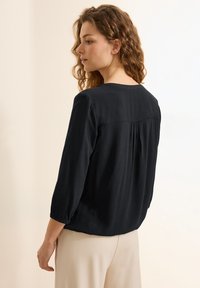 Zwarte blouse met lange mouwen, een ronde halslijn, geplooide achterkant en elastische manchetten, gemaakt van lichtgewicht stof.
