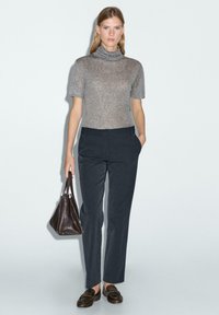 Grijs T-shirt met korte mouwen en col, gecombineerd met donkerblauwe, op maat gemaakte broek. Een bruine leren handtas en loafers maken de outfit compleet.