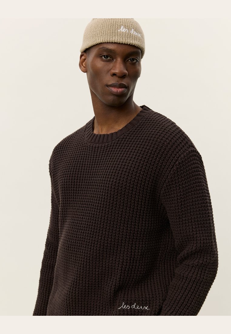 Dark brown textured knit sweater with a round neckline, paired with a light beige knitted beanie featuring white embroidered text.