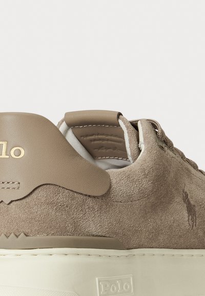 Sneakers bej din suede cu un finisaj texturat, având o talpă din cauciuc alb, cusături contrastante și accente aurii cu logo pe toc și lateral.