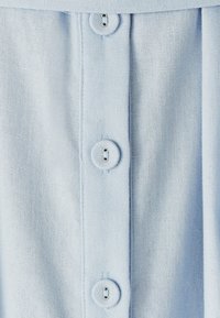 Šviesiai mėlyna medžiaga su tekstūruota paviršiumi, kuriame išilgai priekinės dalies yra penki apvalūs mygtukai ir apykaklėje matomas detalių apipavidalinimas.