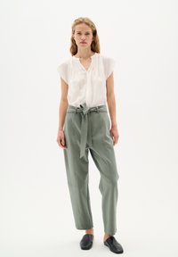 Blusa bianca a maniche corte con abbottonatura. Pantaloni verde salvia a vita alta con cintura legata e cuciture laterali. Scarpe nere slip-on.